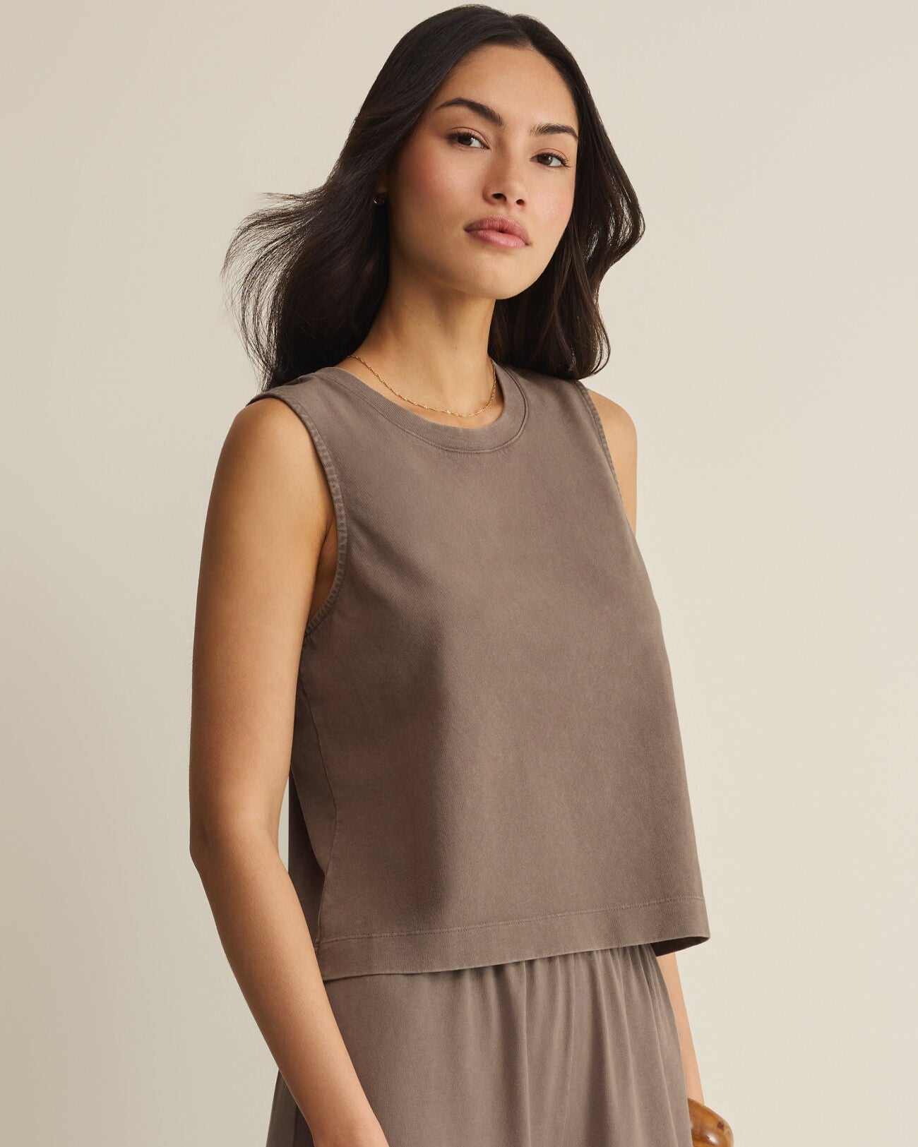 Woman wearing a brown sleeveless top and pants against a beige background