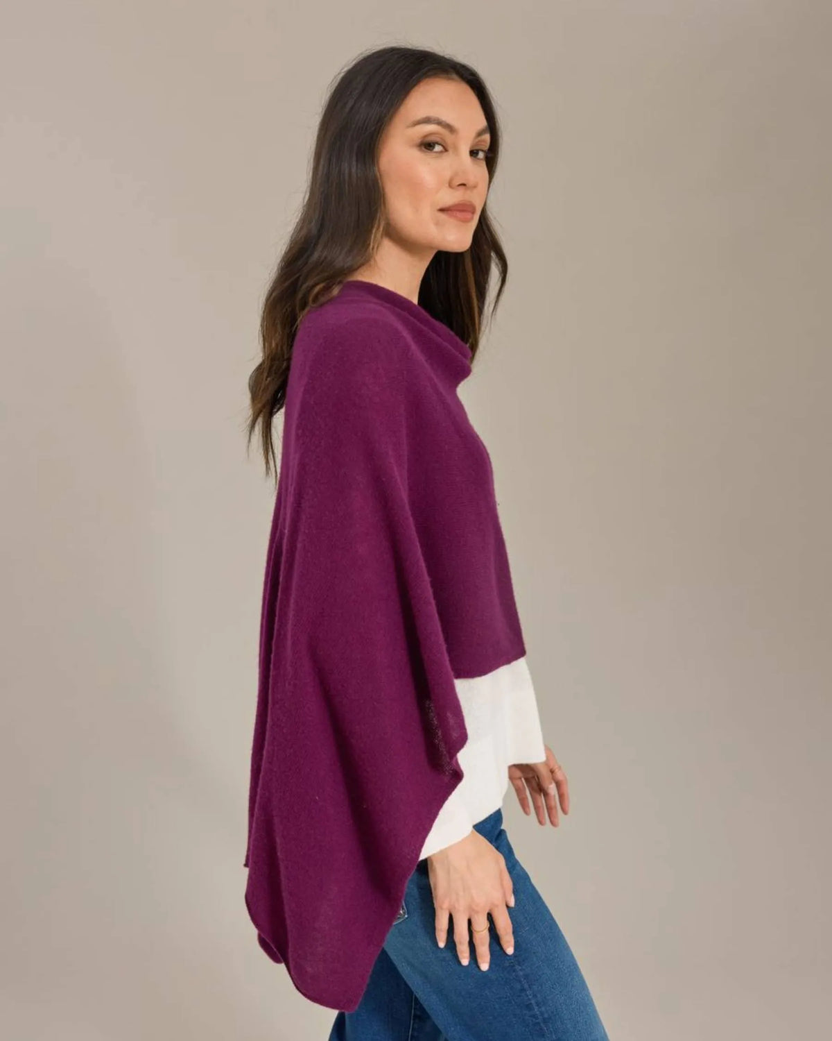 Woman wearing a purple poncho over a white shirt and blue jeans on a beige background