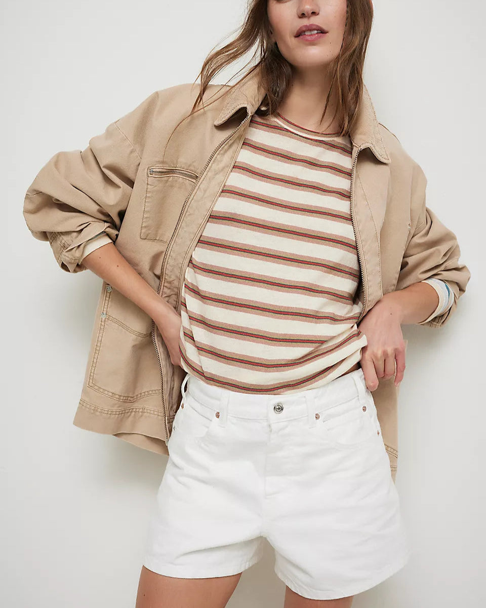 Woman wearing a beige jacket, striped shirt, and white shorts against a plain background