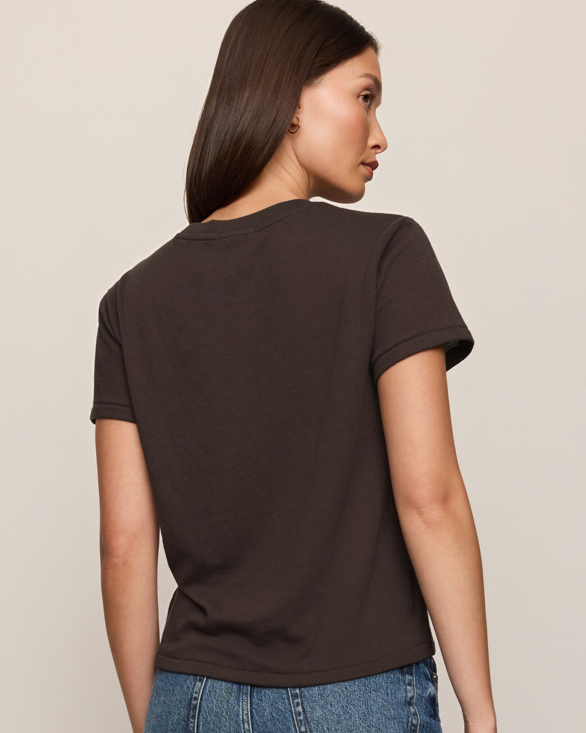 Woman wearing a black t-shirt and blue jeans against a beige background