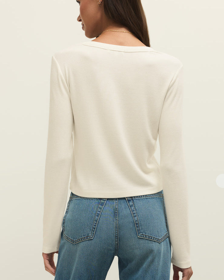 Person wearing a cream long-sleeve top and blue jeans on a plain background