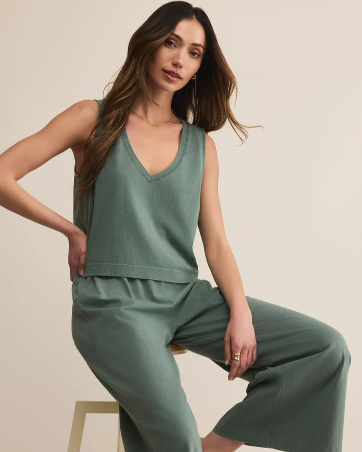 Woman wearing a green sleeveless top and wide-leg pants sitting on a stool against a beige background