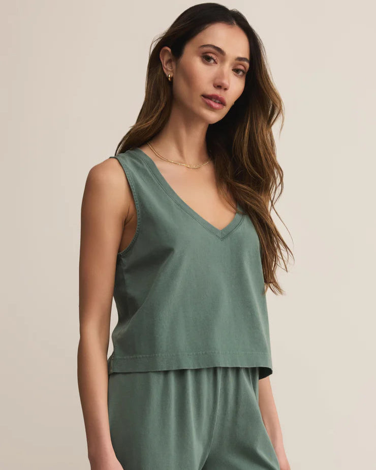 Woman wearing a green sleeveless top and pants against a beige background