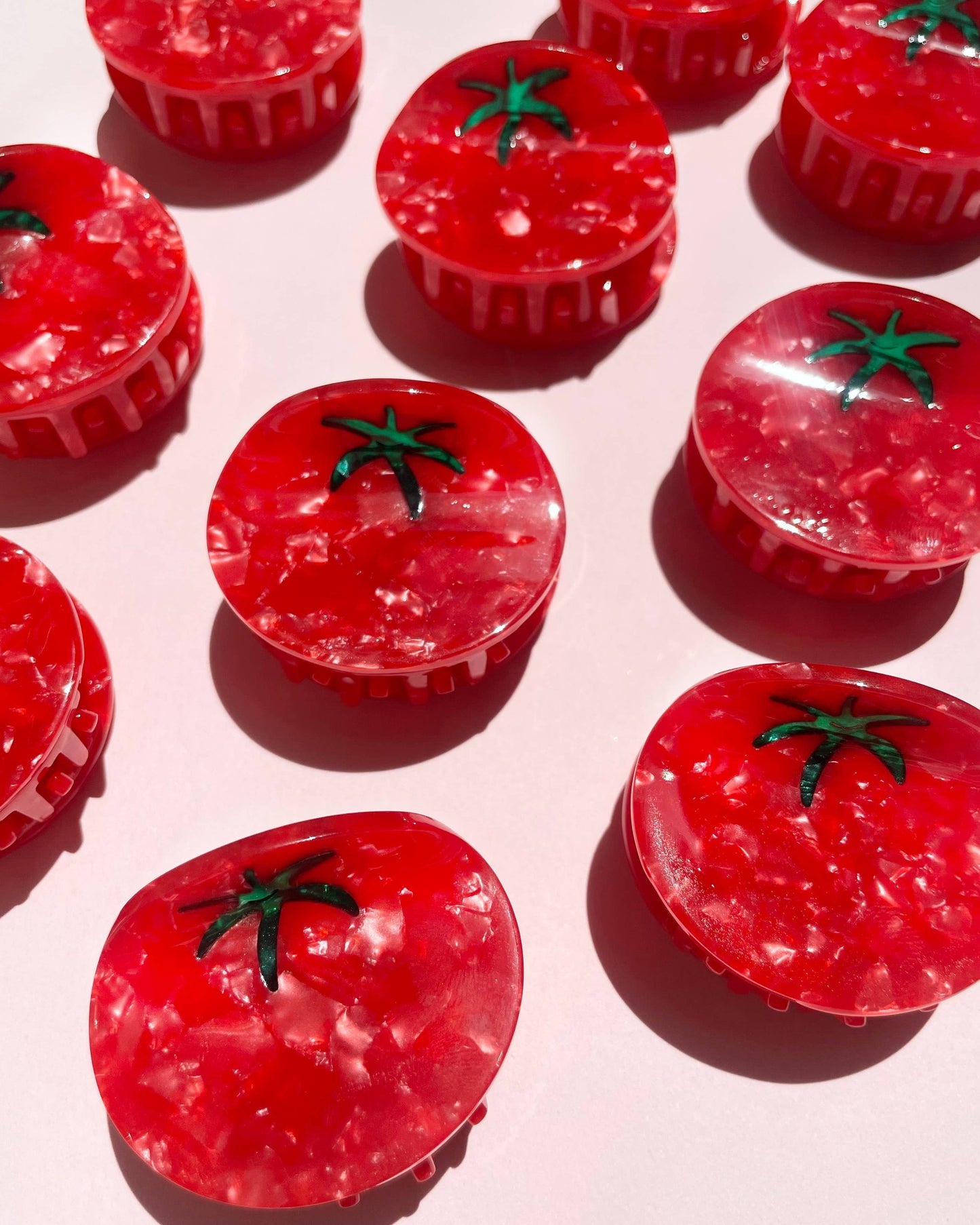 Red tomato-shaped hair clips with green stems on a light pink background