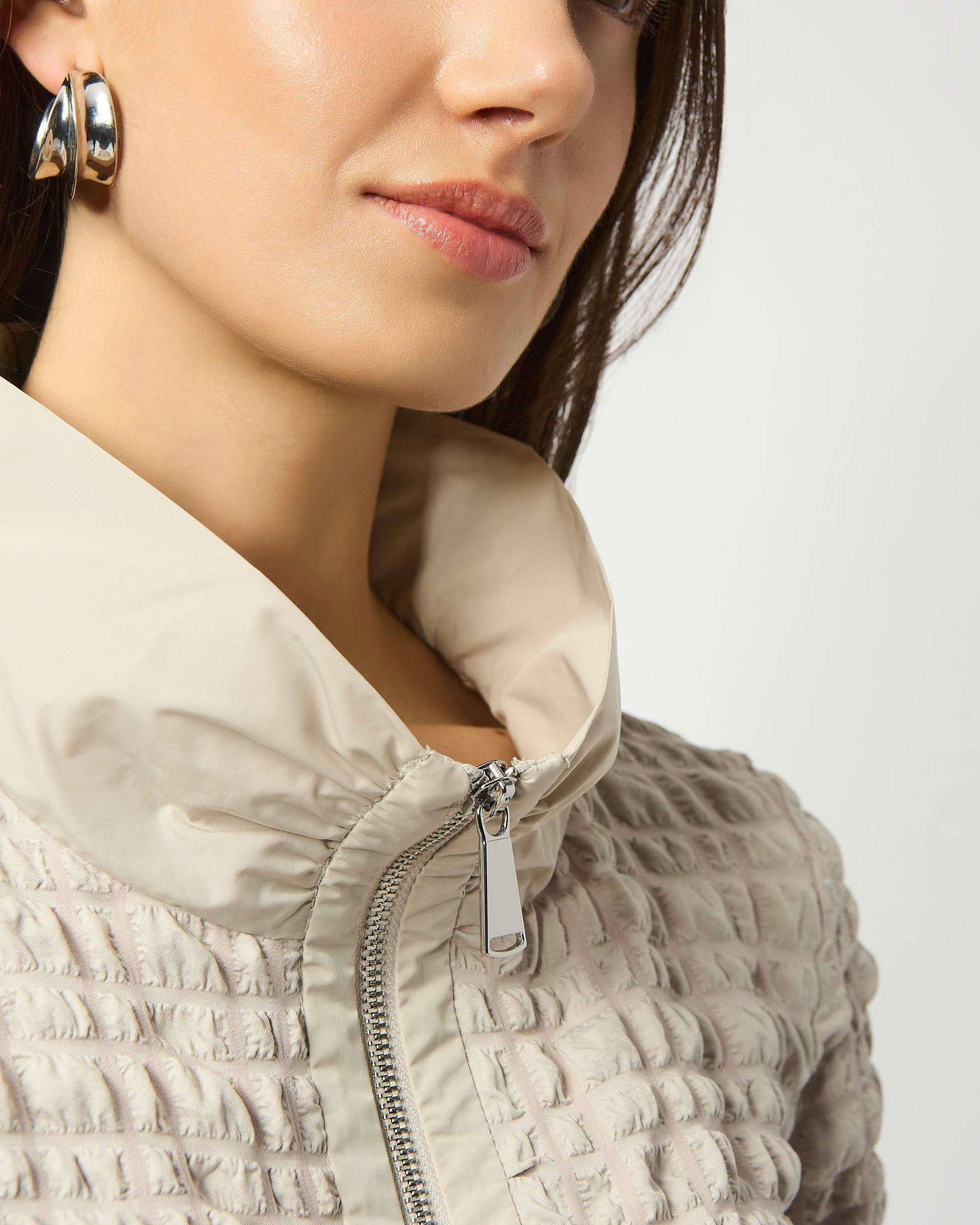 Model is wearing Joseph Ribkoff Bubble Jacquard A-Line Top in color moonstone with silver earrings on a white background