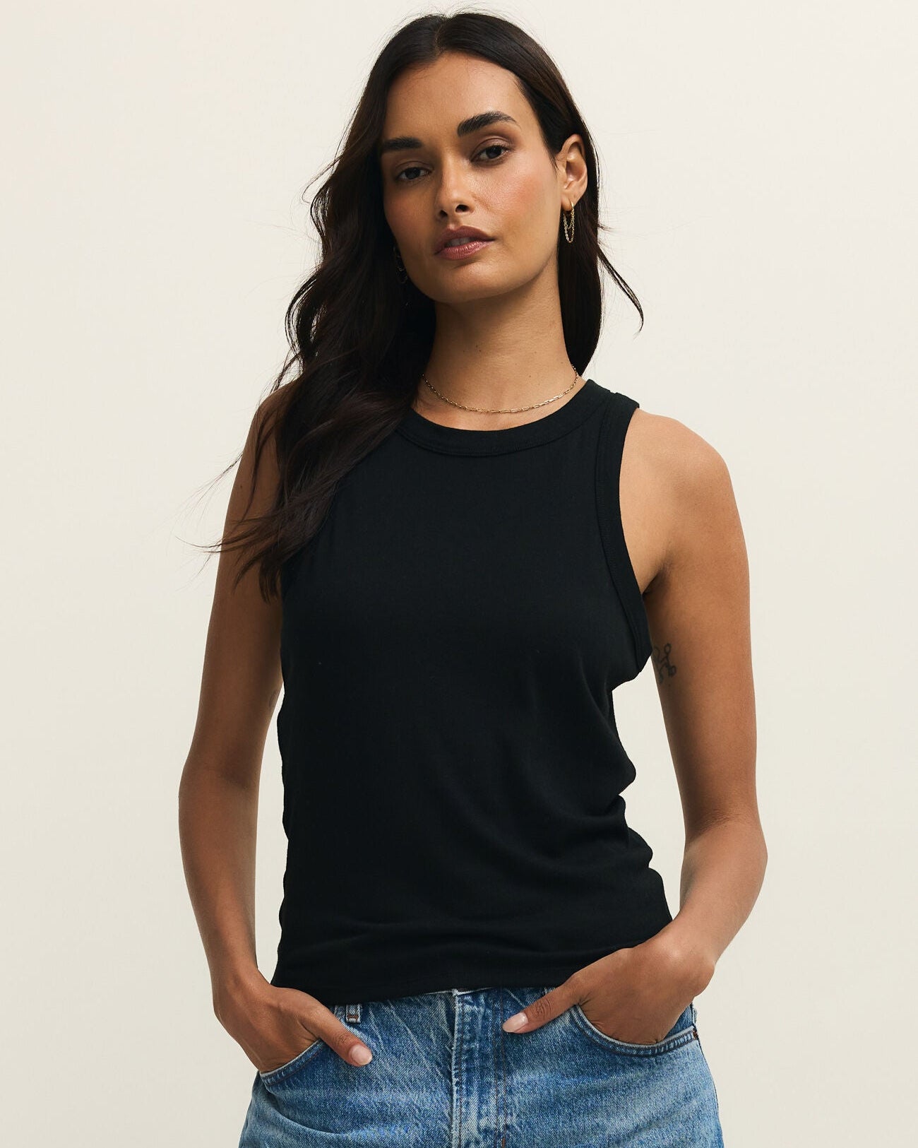 Woman wearing a black sleeveless top and blue jeans against a beige background