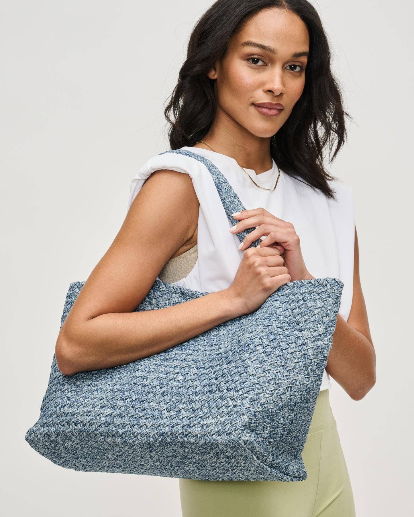 Woman holding a blue textured tote bag against a plain background