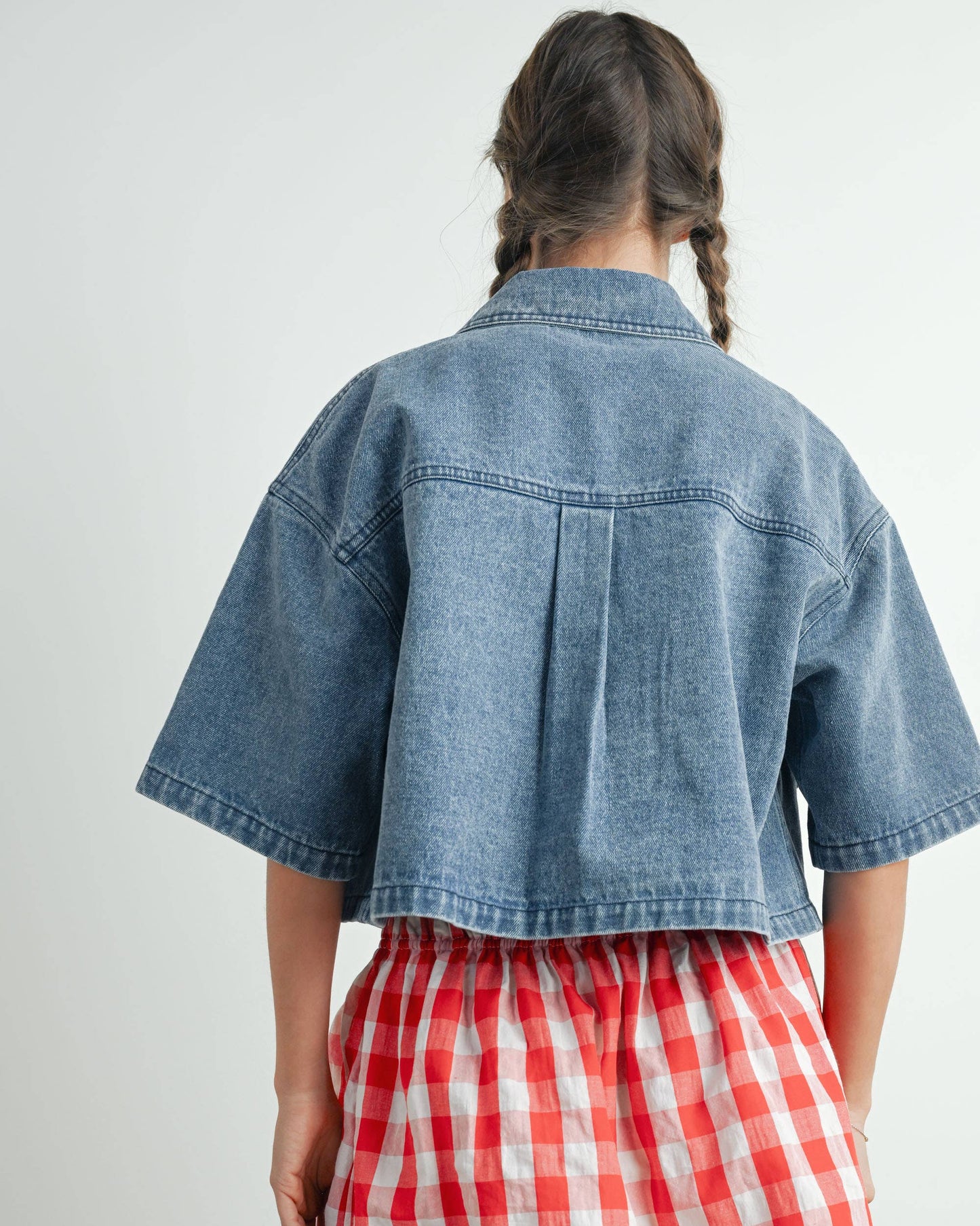 Person wearing a denim jacket and red plaid skirt on a white background