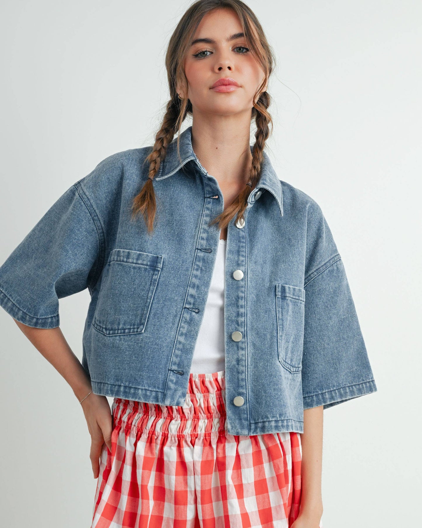 Woman wearing a denim jacket and red checkered shorts on a white background