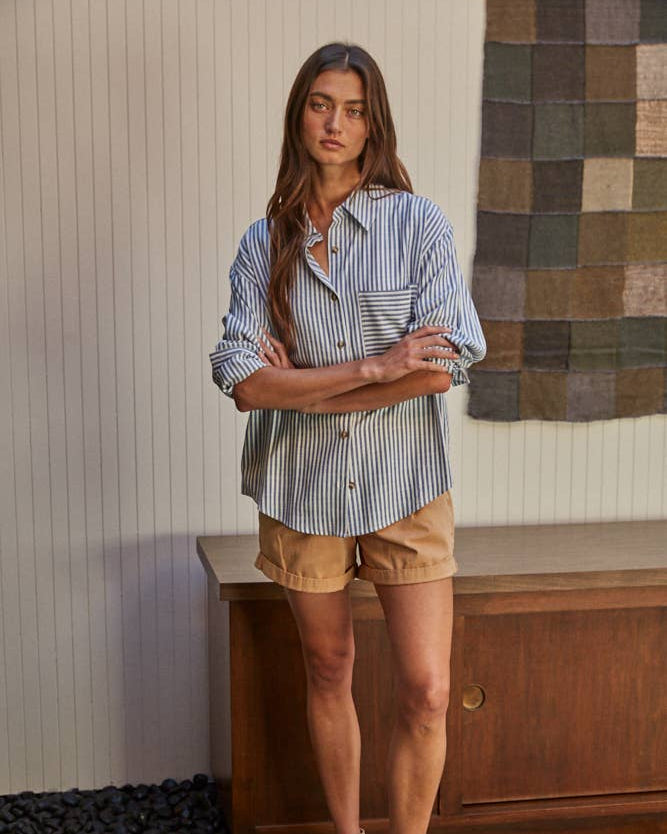Front view of a woman wearing the By Together Woven Cotton Button Down in Blue against a decorated background.