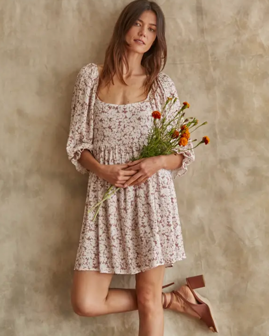 Model wearing By Together Rosy Ruth Dress in rose color holding flowers on a brown background