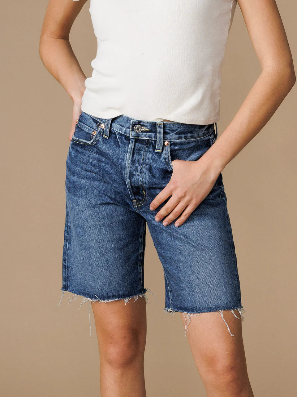 Close up front view of a model wearing the Edwin Sawyer Bermuda shorts in peck and a white tee with their thumb hooked in the front pocket standing in front of a neutral backdrop