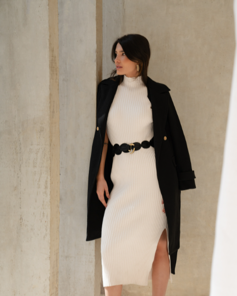 Woman in a white dress with a black jacket standing in a sunlit room.