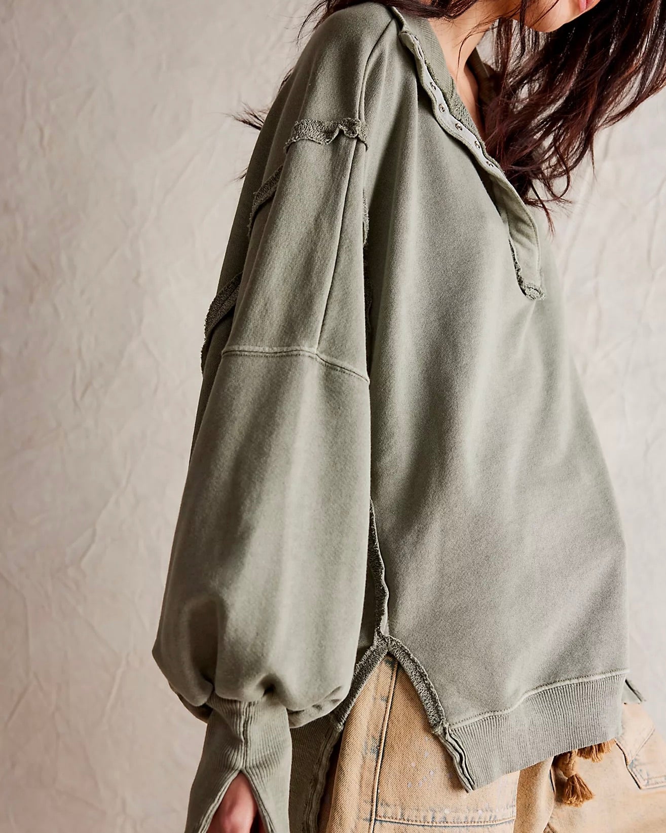Side view of the model wearing the Free People Camden Henley sweatshirt in Laurel Oak showing seam detail, standing in front of a white wall.
