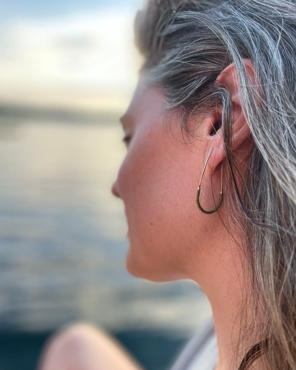 Photo of a model wearing the Wild Balance Waterbury Hoop Earrings in gold with green beads against a blurred background.