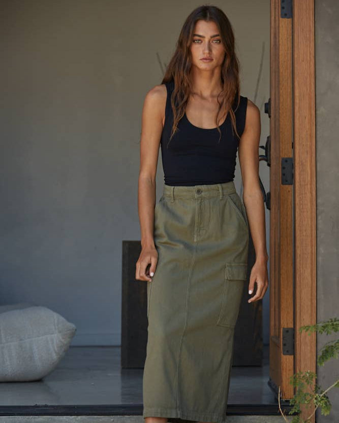 Woman wearing a black tank top and green skirt standing in a doorway.