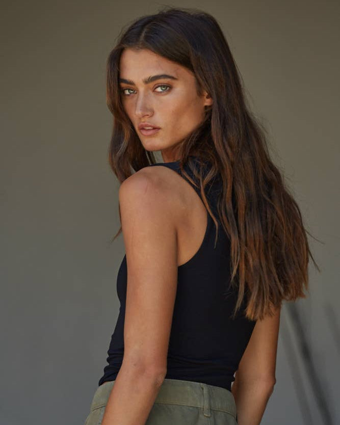 Woman wearing a black sleeveless top and green pants against a neutral background