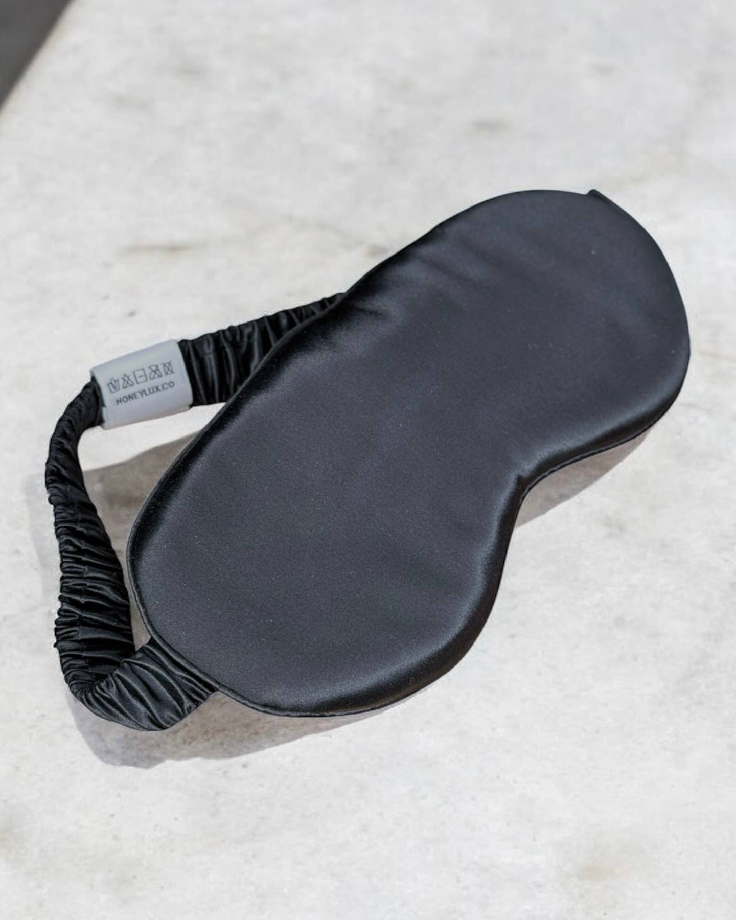 The black silk HoneyLux sleep mask on a neutral background