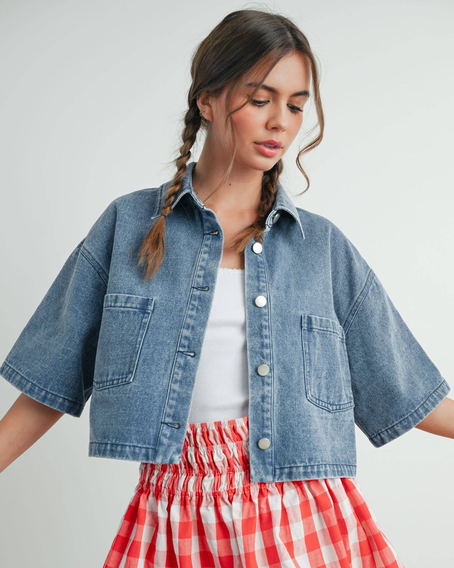 Woman wearing a denim jacket and red checkered skirt on a plain background