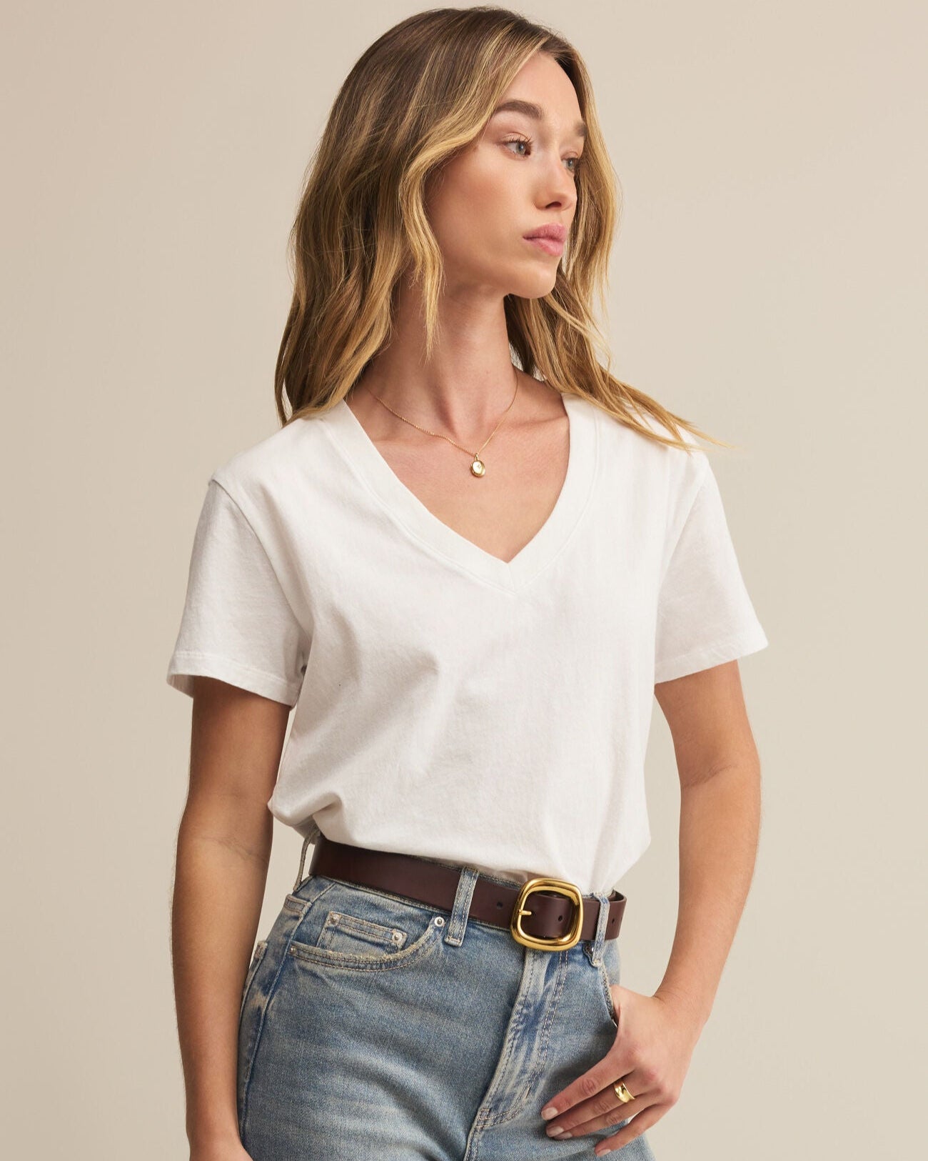 Woman wearing a white t-shirt and blue jeans against a beige background