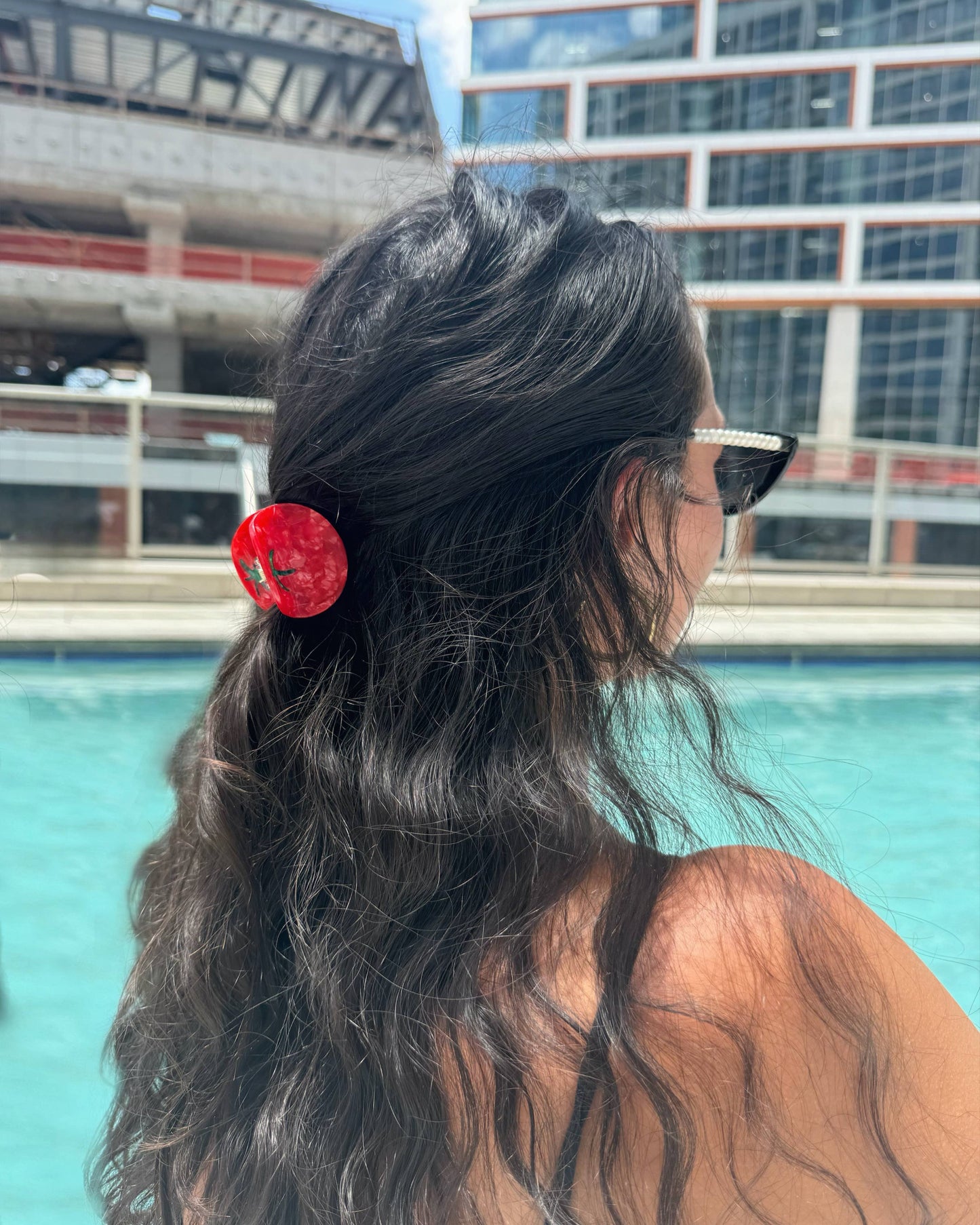 Person with a tomato hair clip by a pool with buildings in the background