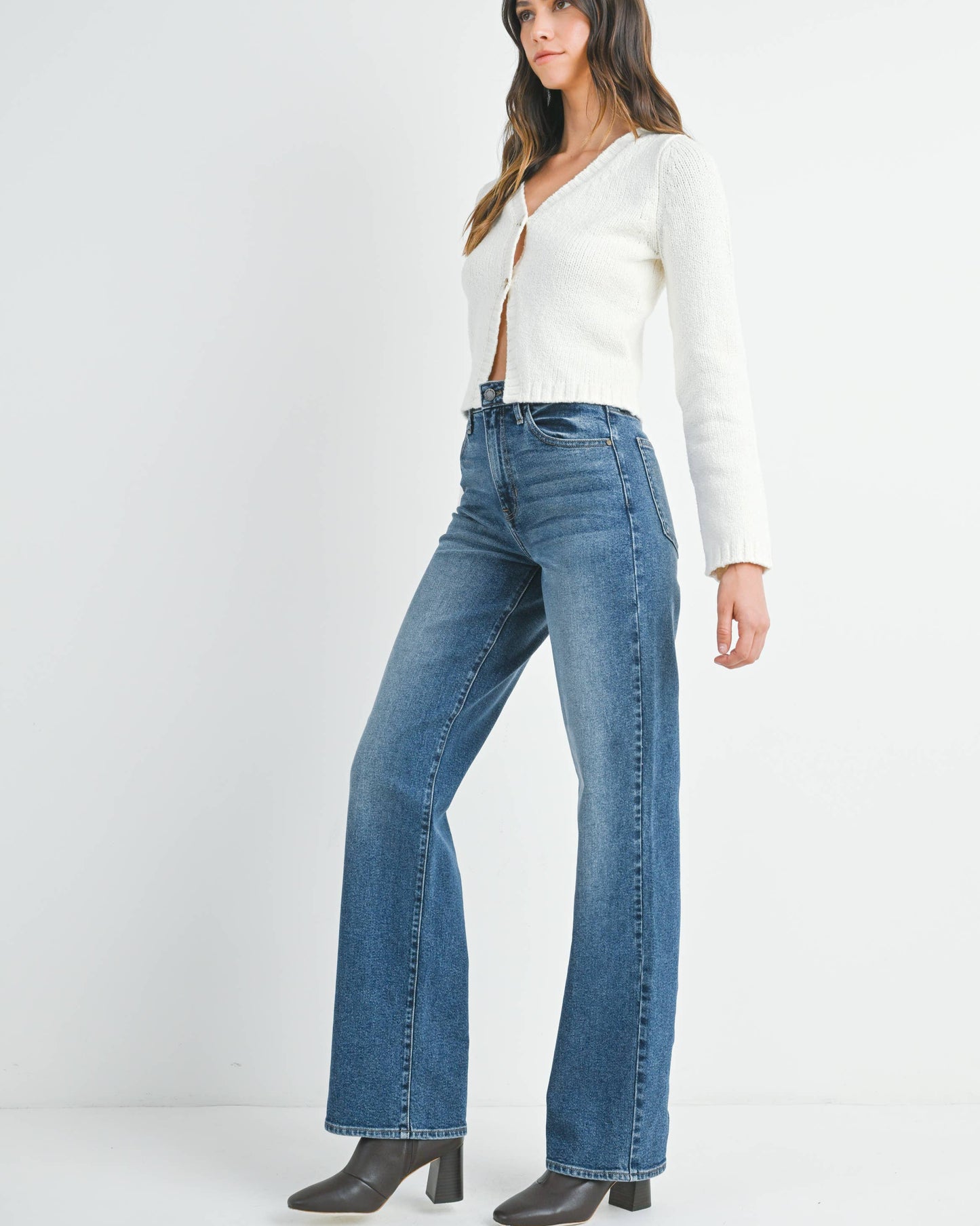 Woman wearing a white long-sleeve top and blue jeans on a white background