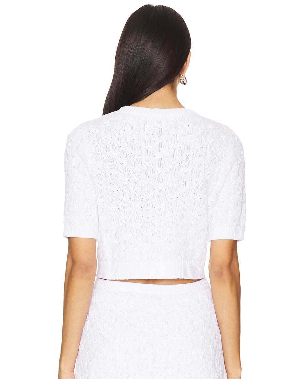 Back view of a model wearing the 525 America Brenda cropped cardigan in bleach standing in front of a white background