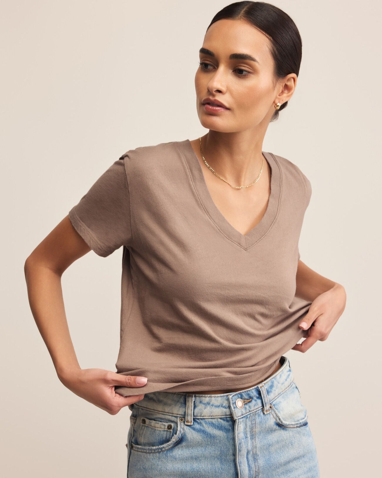 Woman wearing a brown t-shirt and blue jeans against a beige background