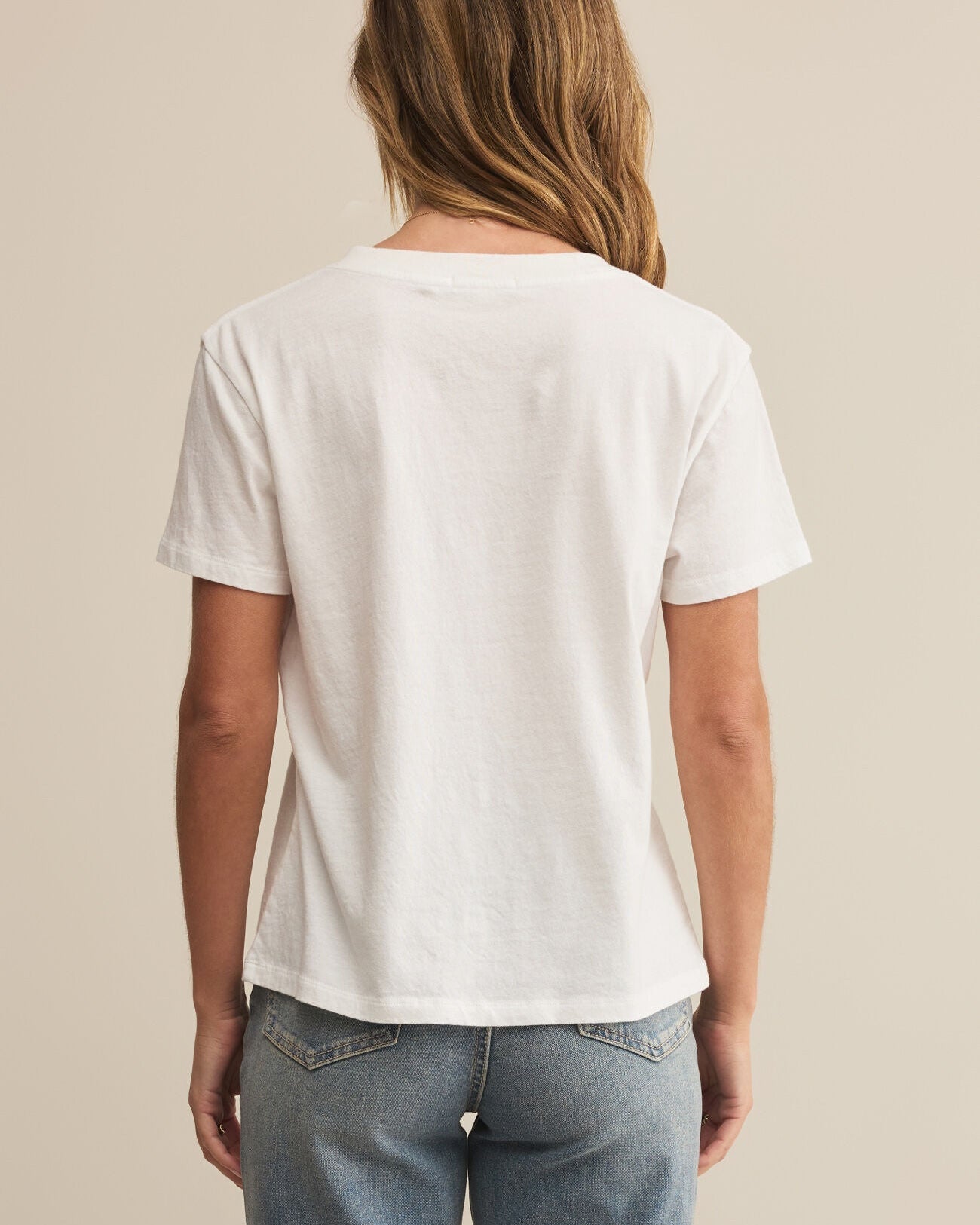 Person wearing a plain white t-shirt and blue jeans on a beige background