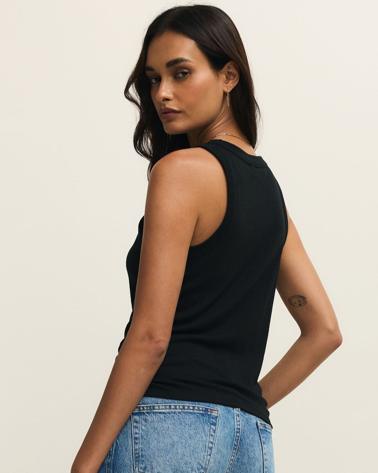Woman wearing a black sleeveless top and blue jeans against a beige background