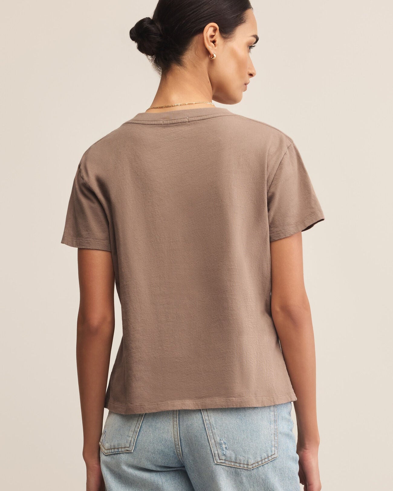 Woman wearing a brown t-shirt and light blue jeans on a beige background