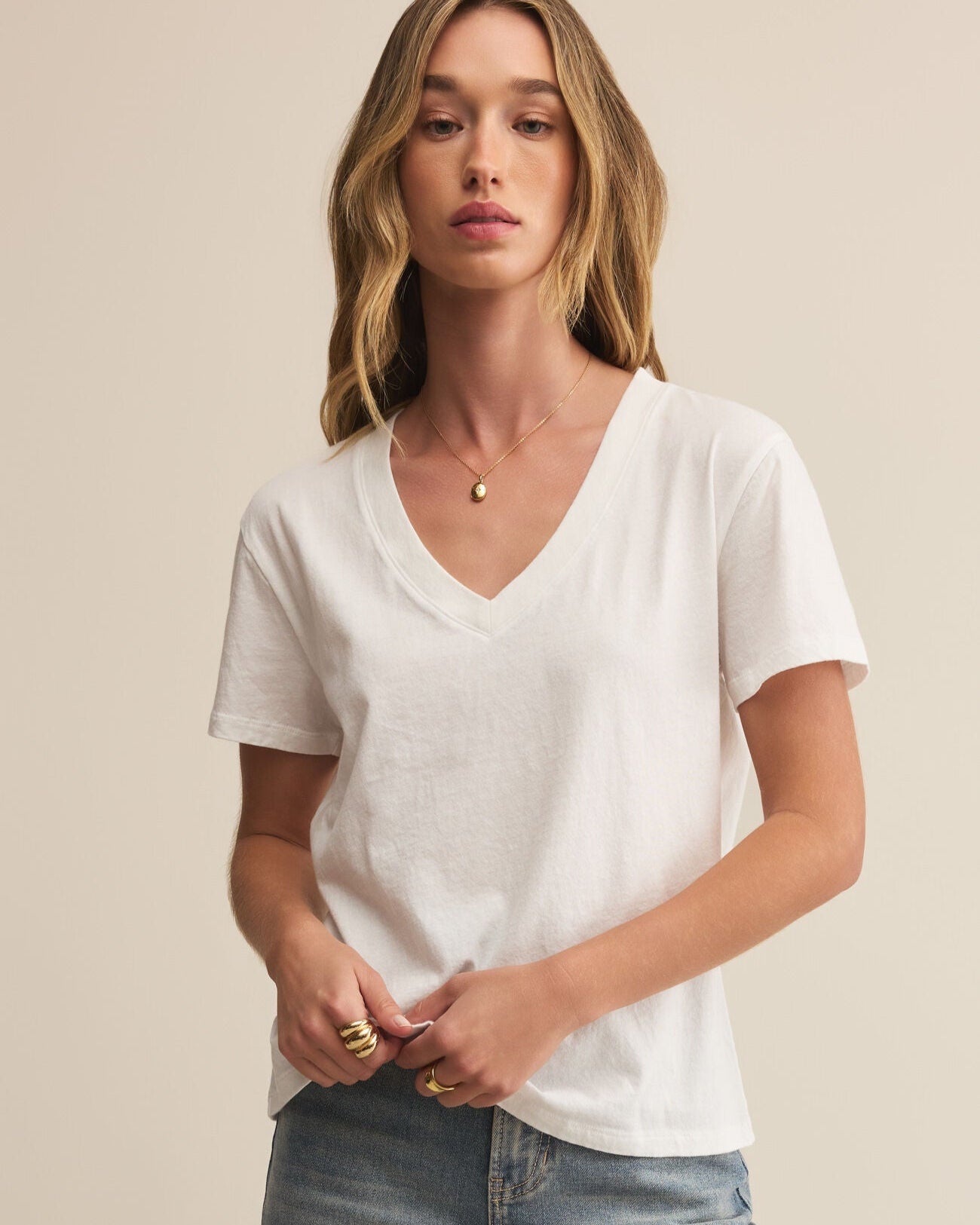 Woman wearing a white t-shirt and light blue jeans against a beige background