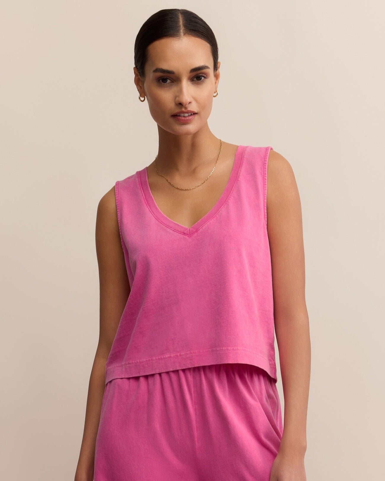 Woman wearing a pink sleeveless top and pants against a beige background
