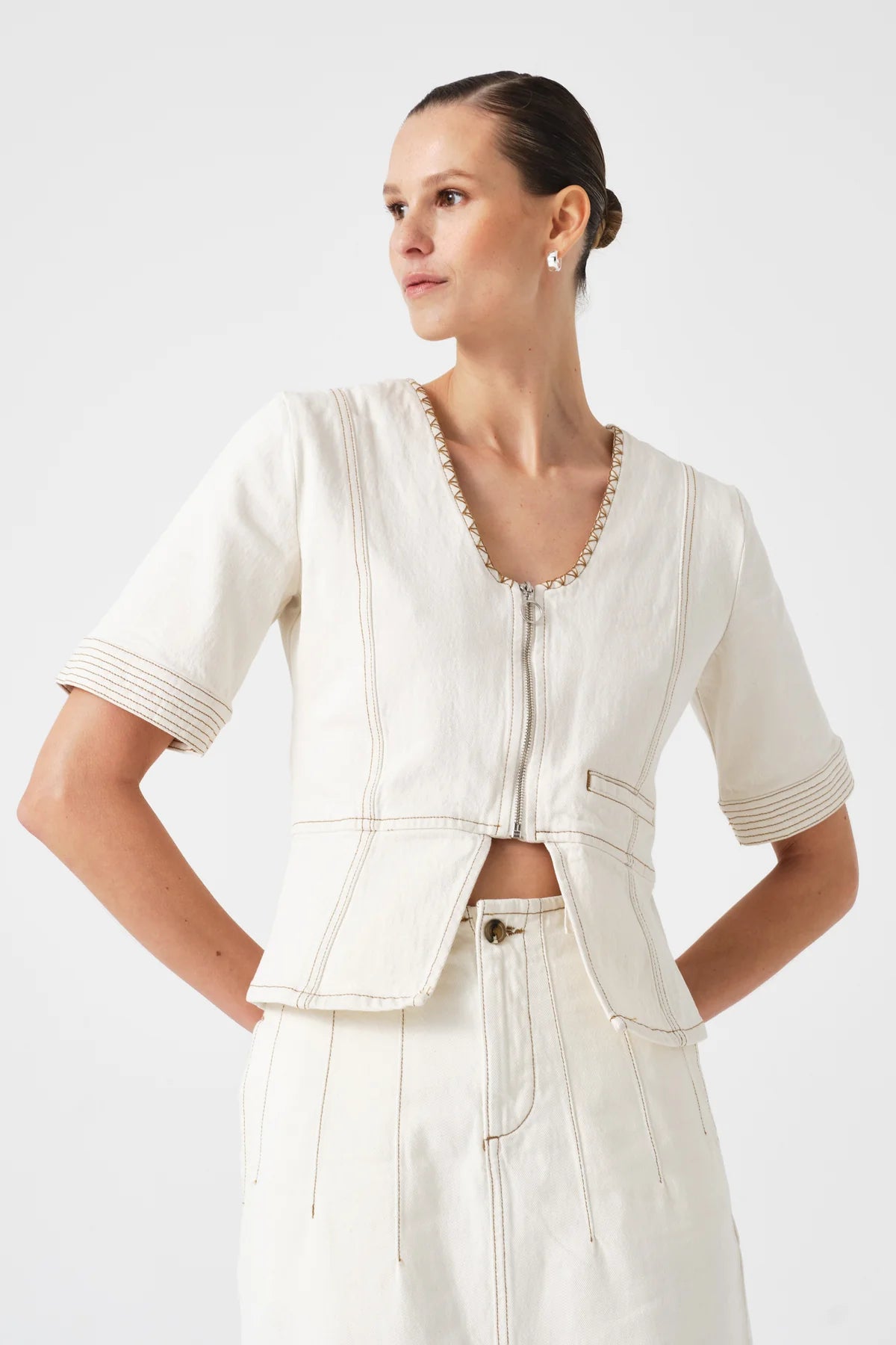 Woman wearing the lea top in ecru with matching skirt on a plain background
