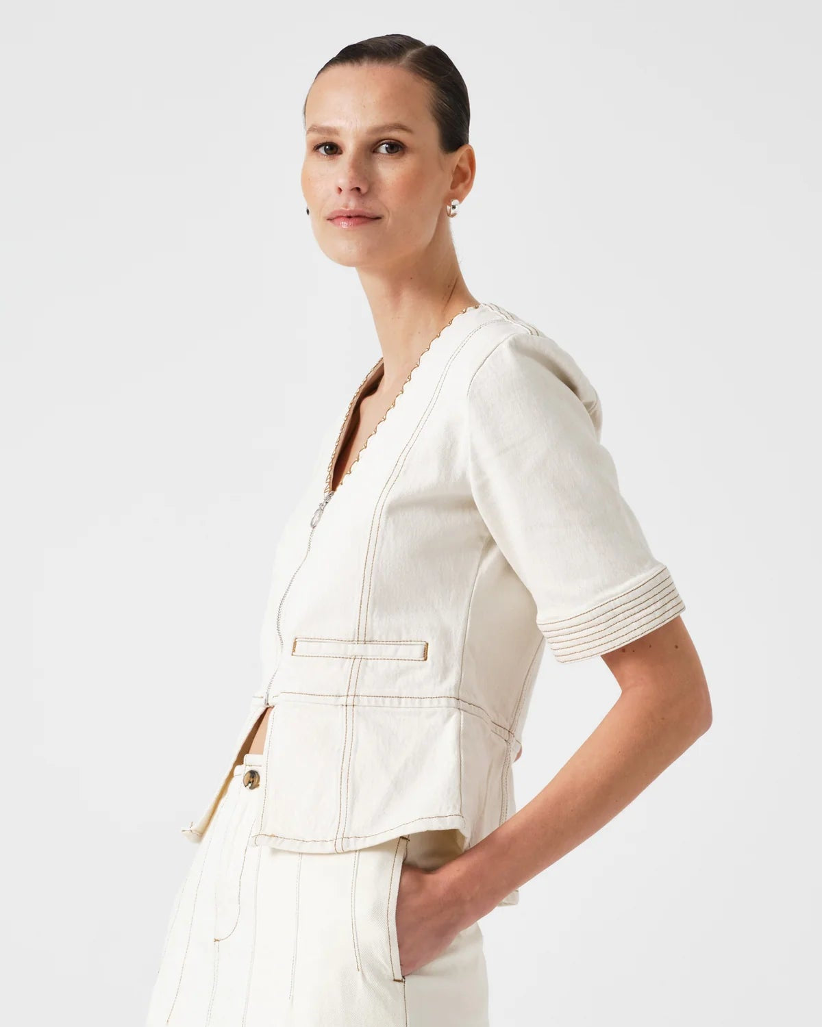 Woman wearing a white outfit with a jacket on a plain background