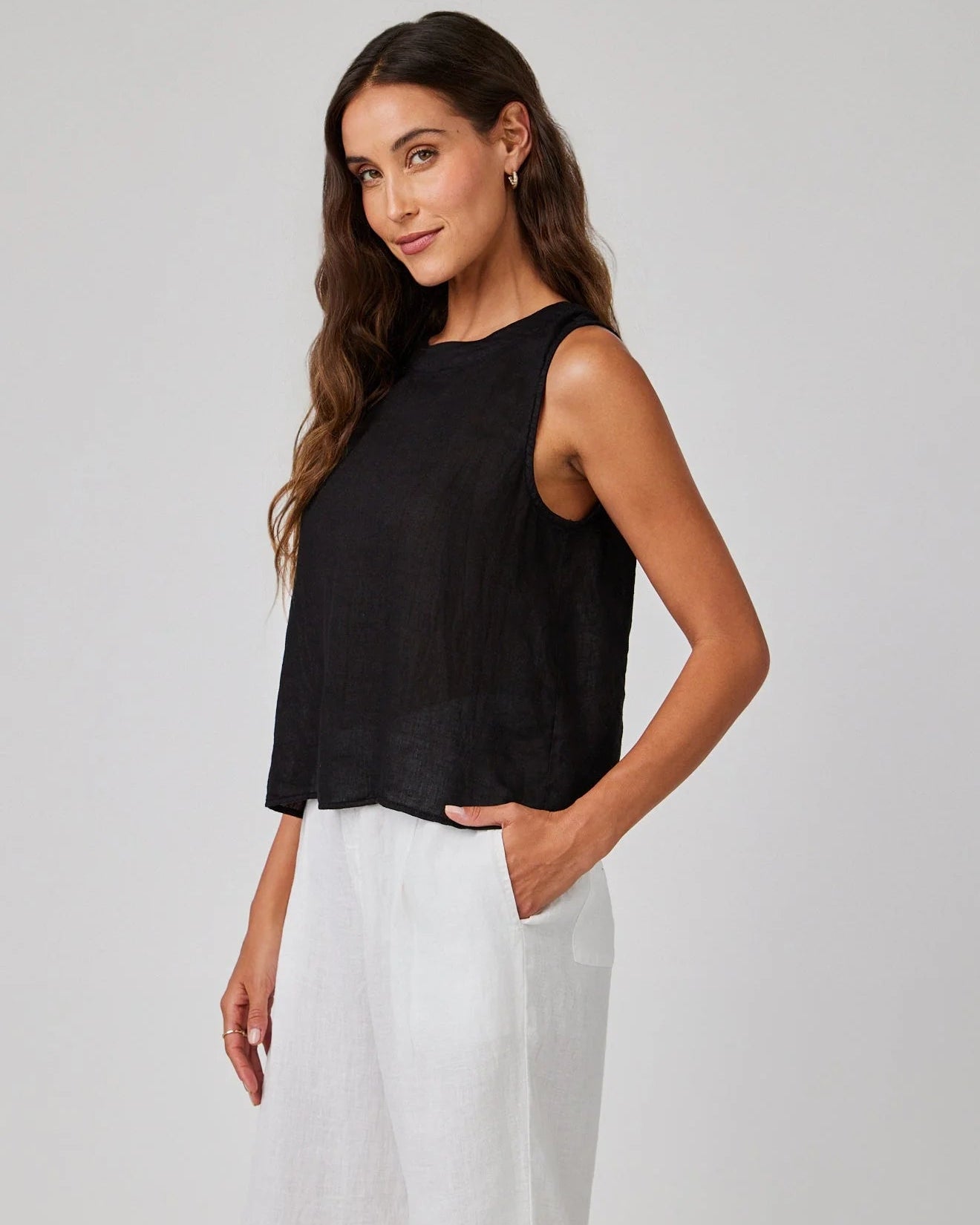 Woman wearing a black sleeveless top and white pants on a plain background