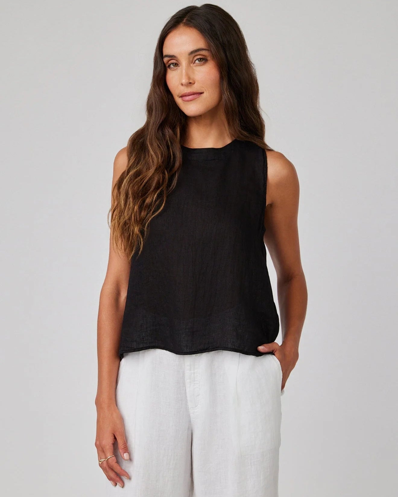 Woman wearing a black sleeveless top and white pants against a plain background