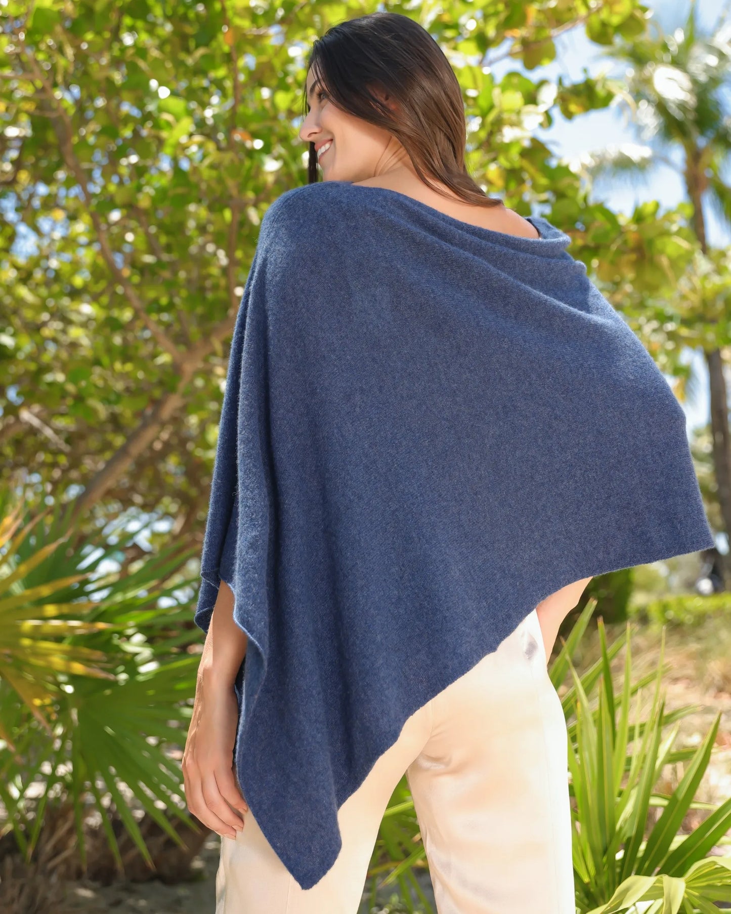 Back view of woman wearing the Alashan Cashmere 100% Cashmere Dress Topper in Denim with plants in the background