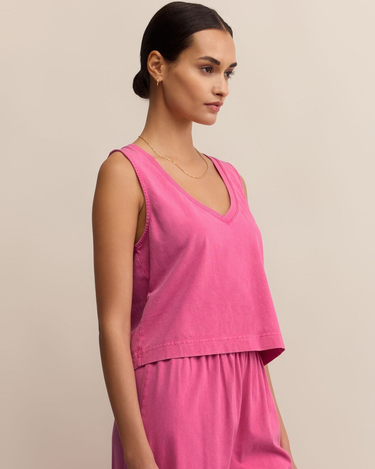 Woman wearing a pink sleeveless top and pants against a beige background