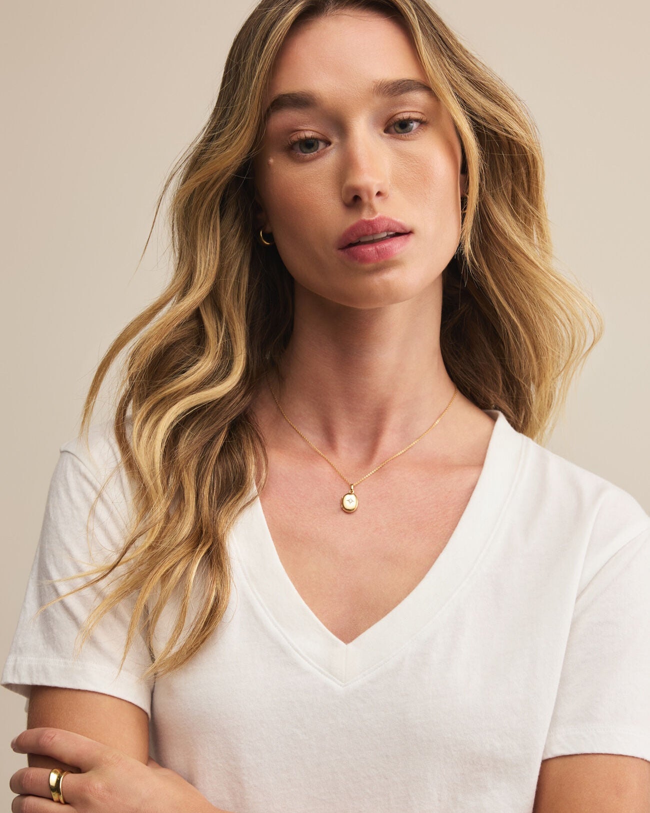 Woman wearing a white shirt and gold necklace against a beige background