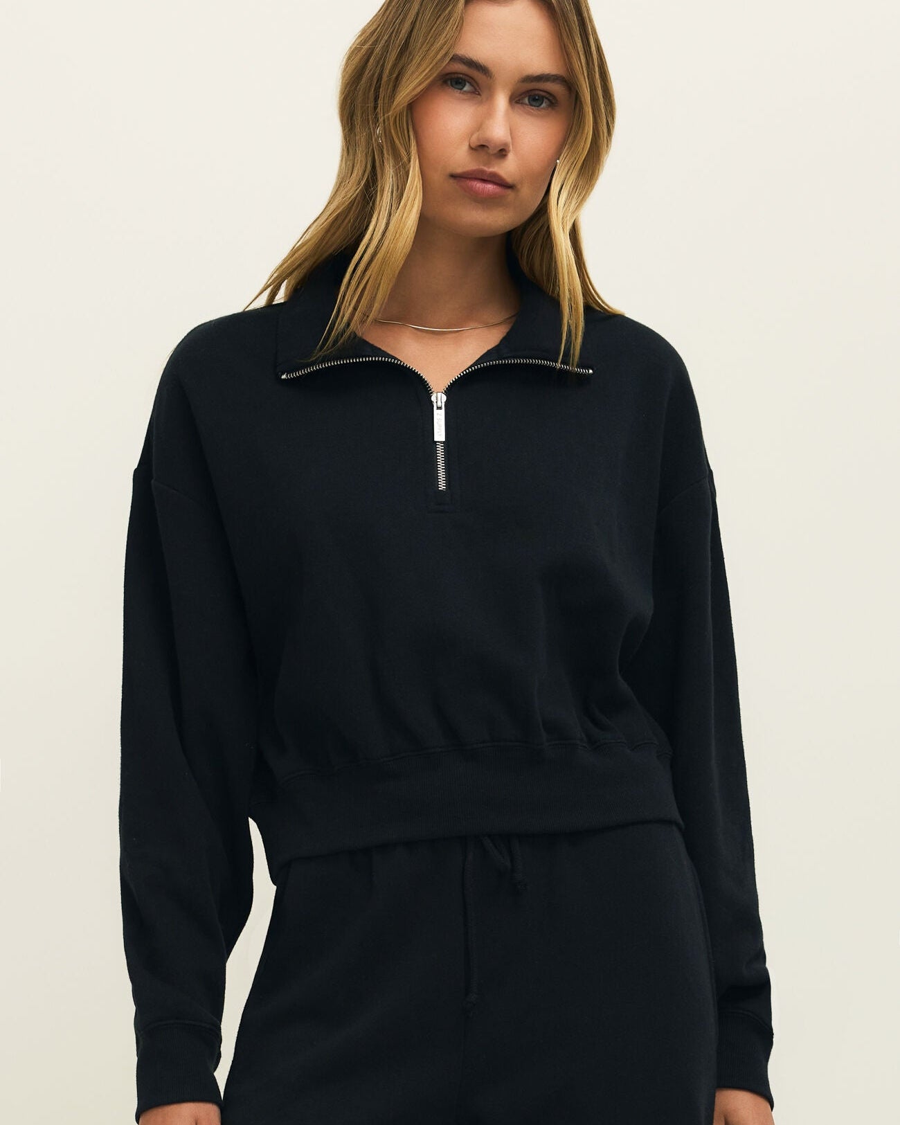Woman wearing a black zip-up sweatshirt and pants on a beige background