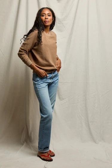Woman wearing a brown sweater and blue jeans against a plain background