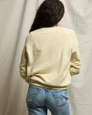 Person wearing a light yellow sweater and blue jeans against a neutral background