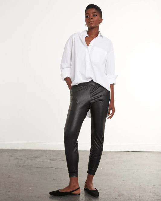 Model Wearing Commando Black Faux Leather Joggers Wearing White Shirt And Black shoes On A White Background