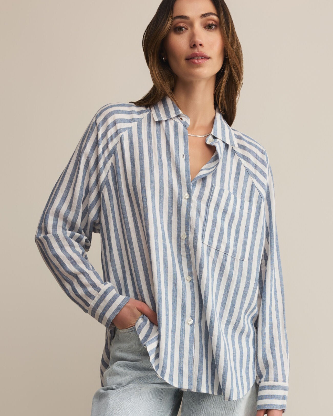 Woman wearing a striped shirt and light jeans against a beige background