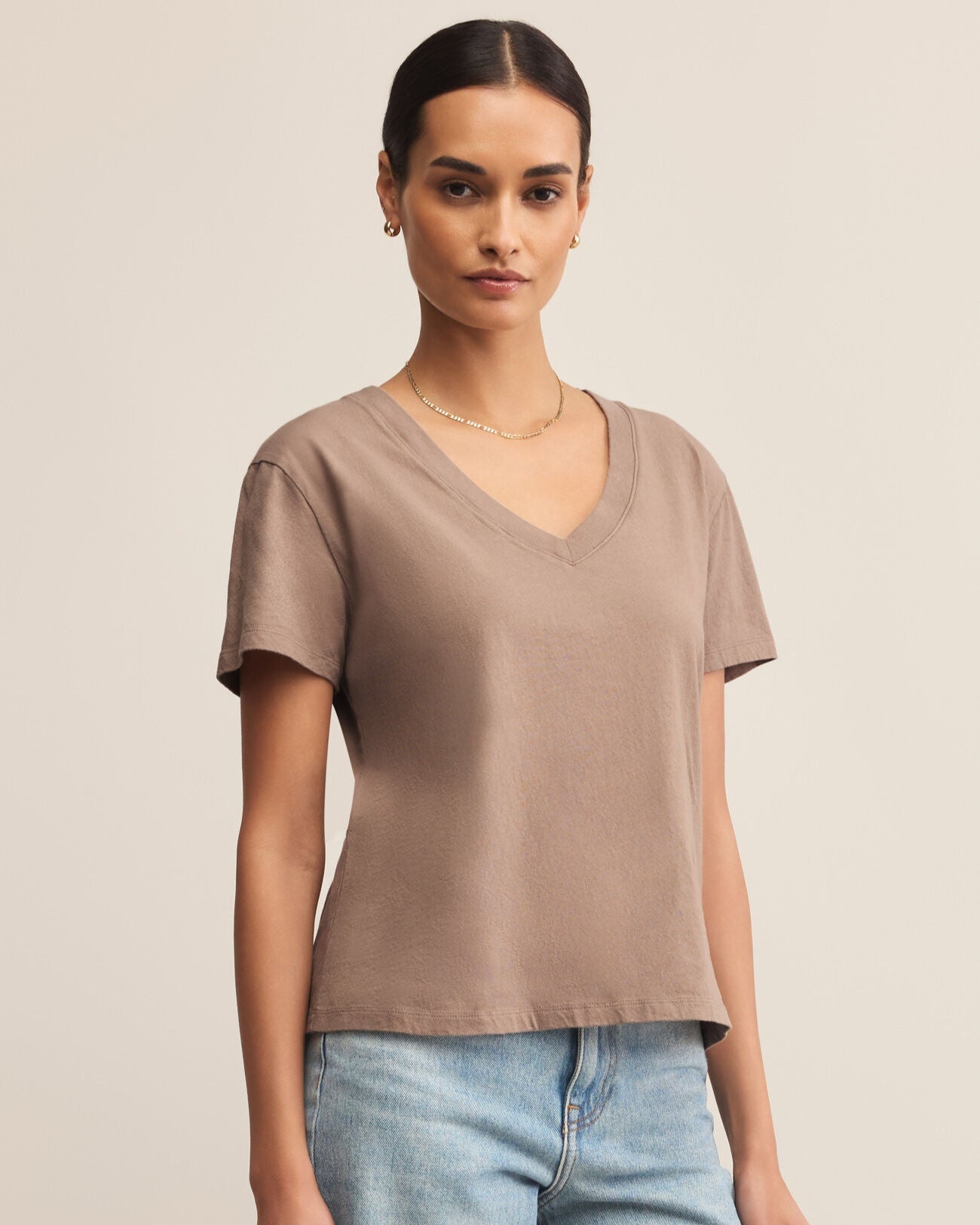 Woman wearing a beige t-shirt and light blue jeans against a beige background