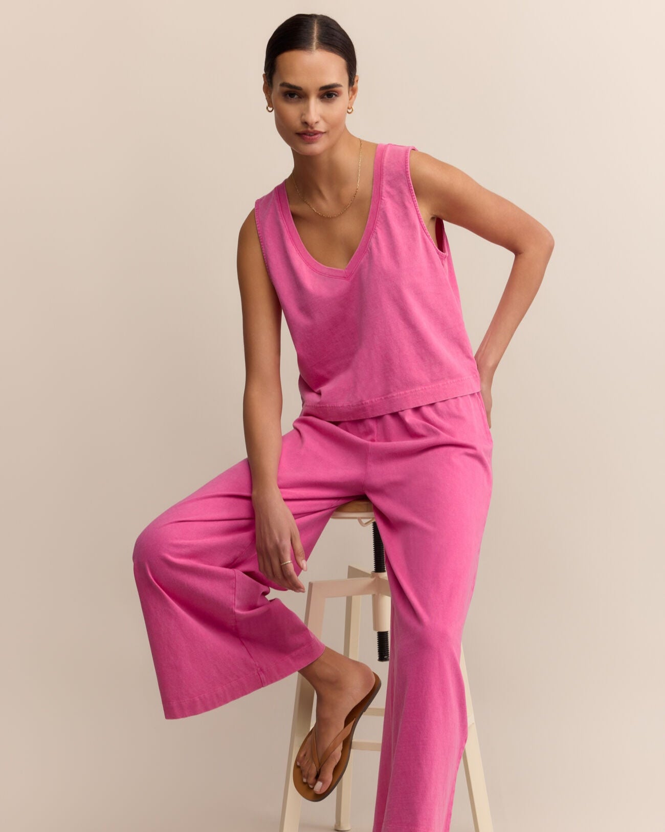 Woman wearing a pink outfit sitting on a stool against a beige background