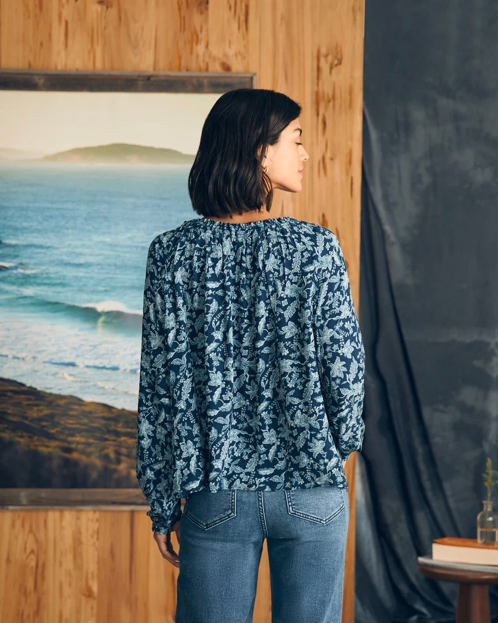 Model wearing Fahery Emery Blouse wearing Jeans standing in front of an ocean painting