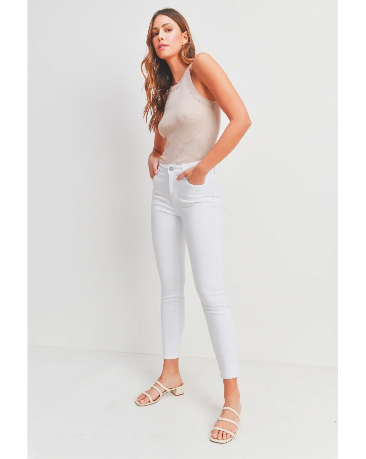 Model Wearing Just Black Denim Modern Classic Skinny Jeans Wearing Beige Tank Top On A White Background