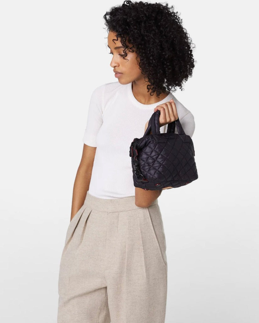 Model Holding MZ Wallace Black Micro Sutton Bag Wearing White Shirt And Gray Pants On A White Background